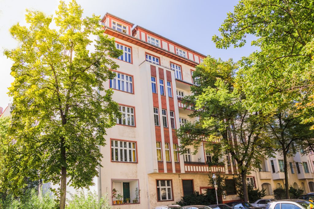 Berliner Wohnhaus mit heller Fassade und grünen Bäumen.